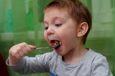 İki yaşındaki güzel bebeğin kaşıkla yemek yemesine yakın durun.