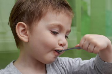 İki yaşındaki güzel bebeğin kaşıkla yemek yemesine yakın durun.