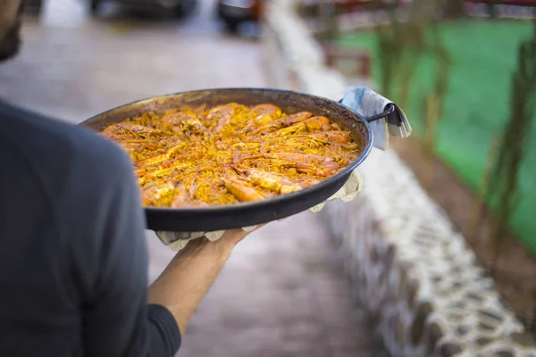 Paella. İspanyol yemeği. Pirinç ve karides ile bir paella taşıyan adam. garson garson