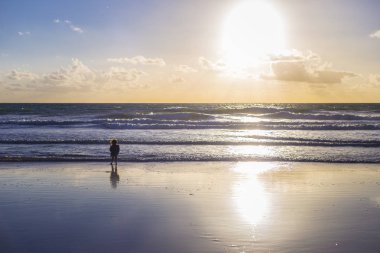 Küçük bir kız su, günbatımında gökyüzünün bulutları tam altında looling silueti ile bir Beach güzel bir manzara,