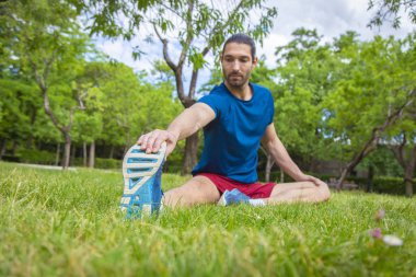 Genç adam çim yaz parkta oturup bacak Germe