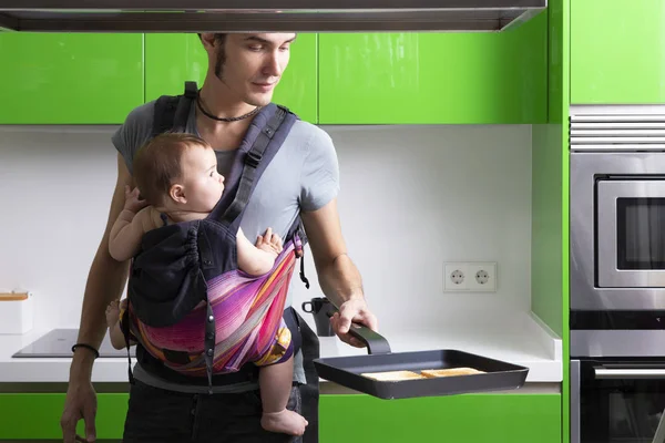 young father making coffee with his baby in carrier in green modern kitchen