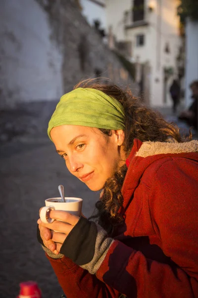 beautiful young woman with a green handkerchief and red coat, having a coffe in the street in a sunny afternoon in Granada, Spain.