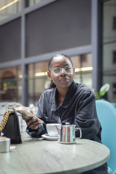 Atractiva Mujer Africana Joven Usando Teléfono Inteligente Mientras Toma Una —  Fotos de Stock