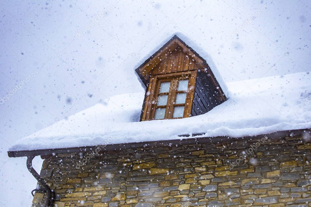 Roof of a house with a window covered with snow in a snowy day