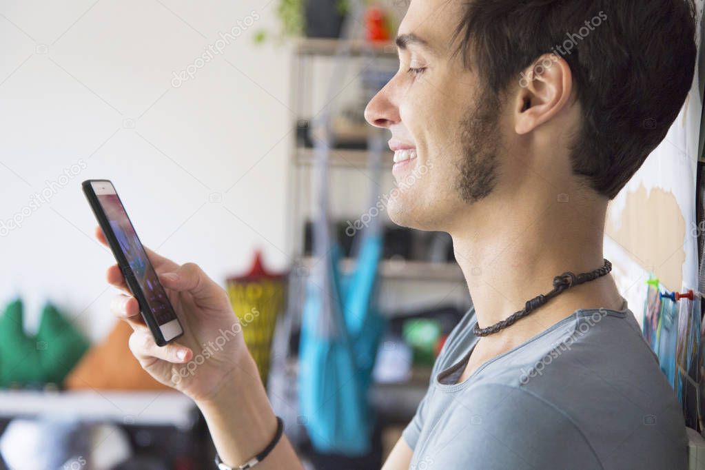 Whatsapp or tinder date. Young caucasian man smiling while using a smartphone at home
