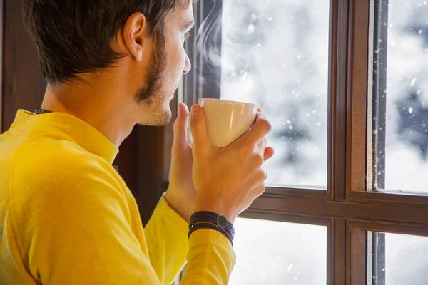 Kış sahne. Genç adam, kar pencereden bakarken sıcak bir kahve sarı giyinmiş