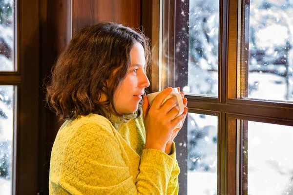 Kış sahne. Sarı kar pencereden bakarken sıcak bir kahve ile genç bir kadın giyinmiş