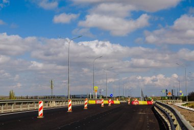 Mavi gökyüzü ve beyaz bulutlar üzerinde yol lambaları olan yeni asfalt yol.