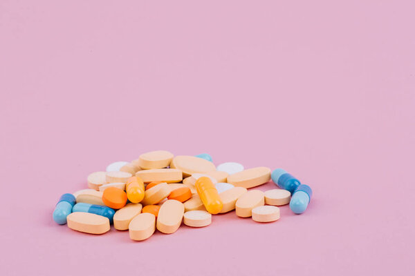 Assorted pharmaceutical medicine pills, tablets and capsules on a pink background. A colorful pile of pills.