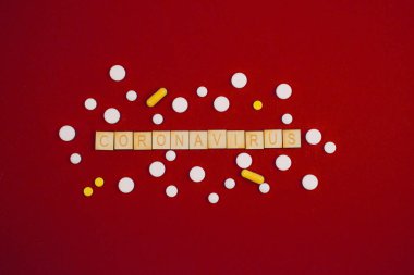 Kırmızı arka planda tahta küplere Coronavirus yazıtı ve çeşitli haplar. Sağlık kavramı.