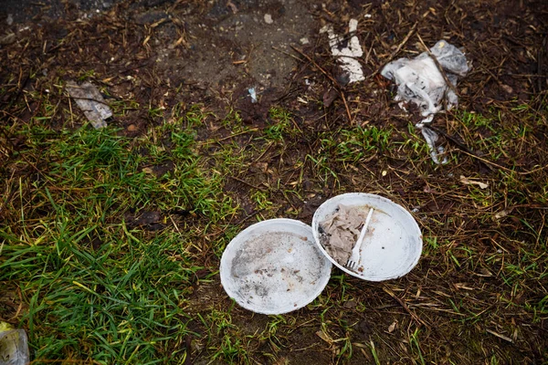 Disposable plastic dishes have long been left in the woods. White plastic slippers, forks are thrown to the ground. Garbage in the forest. The problem of plastic waste pollution.
