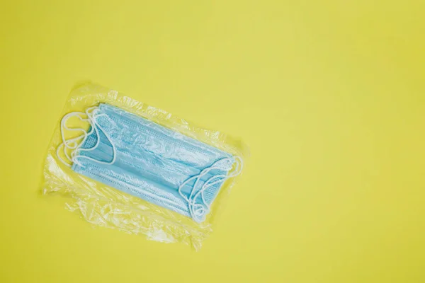 Packaging surgical masks with rubber ear straps on a yellow background. A disposable surgical face mask closes the mouth and nose. The concept of protection against bacteria and viruses. Copy space