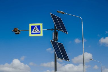 Güneş panellerinden güç alan yaya geçidi tabelası yukarıda. Trafik işaretleri ve kurallar. Arkaplanda bulutlu mavi bir gökyüzü 