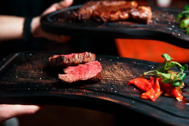 Tahta bir tahtada servis edilen lezzetli ve sulu biftek dilimleri. Tuz, sebze ve otlarla servis edilir..