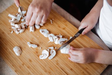 Tahtada taze şampiyon mantarları. Bir kız ve annesi bıçakla mantar kesiyor. Birlikte geçirdiğimiz zaman. Aile kavramı