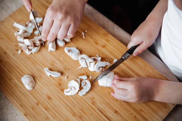 Tahtada taze şampiyon mantarları. Bir kız ve annesi bıçakla mantar kesiyor. Birlikte geçirdiğimiz zaman. Aile kavramı