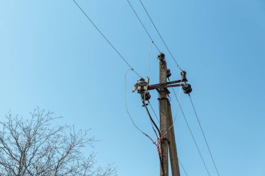  Elektrik kablolarıyla elektrik direği beyaz bulutlu, berrak bir gökyüzüne karşı. Sütunun yanında bir ağaç yetişiyor. Elektrik iletim hattı, güç kaynağı