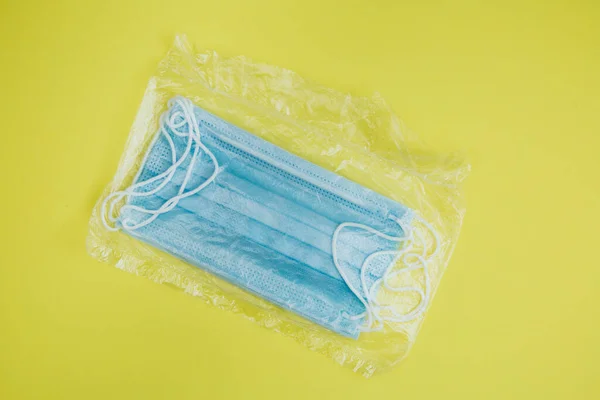 Packaging surgical masks with rubber ear straps on a yellow background. A disposable surgical face mask closes the mouth and nose. The concept of protection against bacteria and viruses.