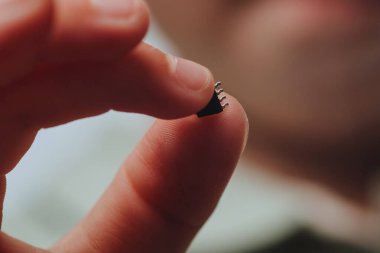 Bir kız elinde tutuyor ve küçük siyah bir çipi inceliyor. Salgın bir koronavirüsten sonra insanların yontulması. Kapat.