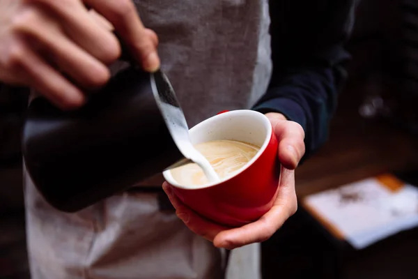 Barista bir fincan kahveye taze süt koyar. Çiçek Latte sanatı.