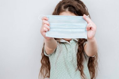 Bir kız elinde tıbbi bir maske tutuyor. Enfeksiyonun önlenmesi ve koronavirüsün yayılması, karantina.