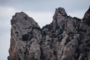 Taş tepeler ve dağlar, yeşil ağaçlar ve çalılar gökyüzüne karşı..