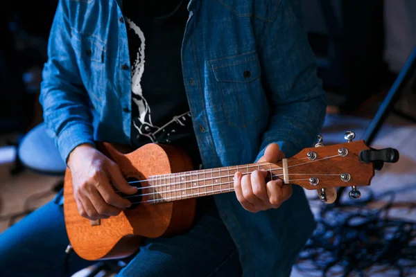Genç bir adam otururken gitar çalar. Ukulele oyunu