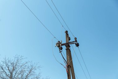  Elektrik kablolarıyla elektrik direği beyaz bulutlu, berrak bir gökyüzüne karşı. Sütunun yanında bir ağaç yetişiyor. Elektrik iletim hattı, güç kaynağı