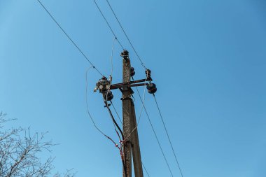 Elektrik kablolarıyla elektrik direği beyaz bulutlu, berrak bir gökyüzüne karşı. Sütunun yanında bir ağaç yetişiyor. Elektrik iletim hattı, güç kaynağı