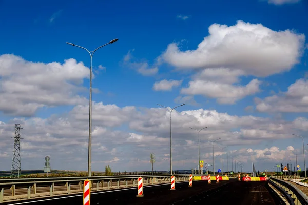 New asphalt road with road lamps on a background of blue sky with white clouds.