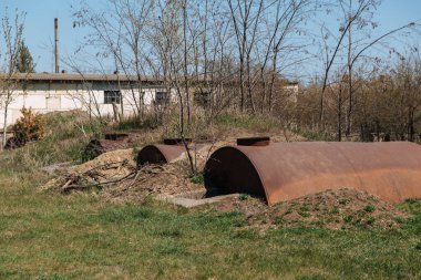 Eski terk edilmiş paslı varillerin yarısı toprağa gömülüdür.