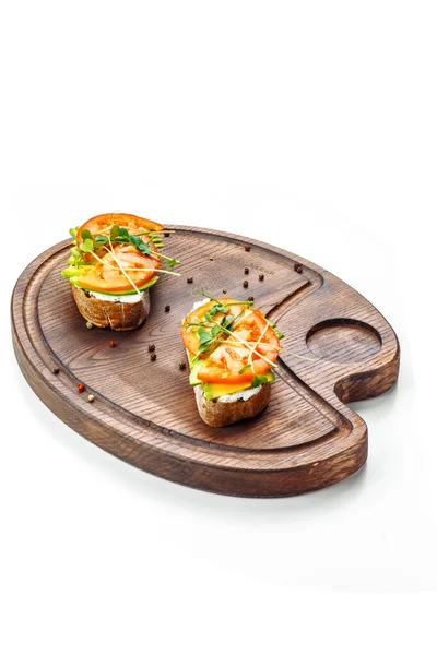 Bruschetta s rajčatovým krémem a avokádem leží na dřevěné desce. — Stock fotografie