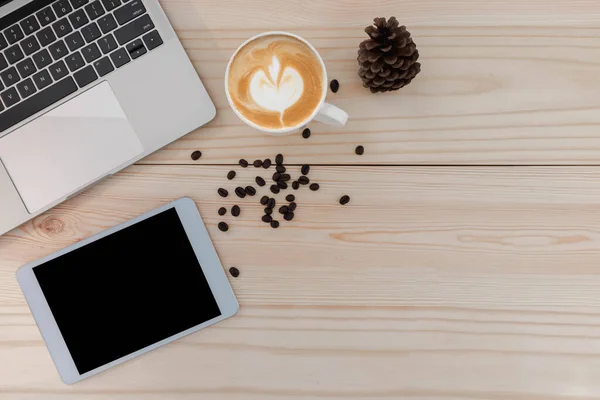 The top view of the mockup tablet is on the notebook, with a pen and notebook and a coffee latte on a wooden table.