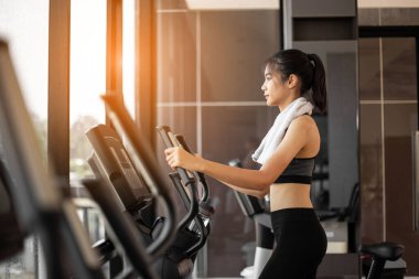 Genç bir kadın spor salonunda eliptik antrenörle egzersiz yapıyor..
