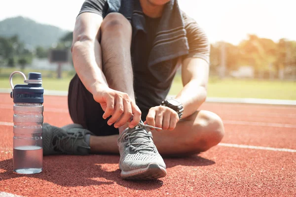 Stadyumda ayakkabı bağı bağlayan bir koşucu..