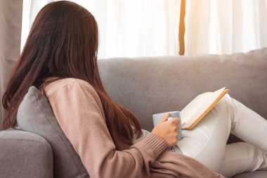 Kitap okuyan ve elinde kahve fincanı tutan genç bir kadın..