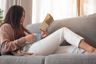 Kitap okuyan ve elinde kahve fincanı tutan genç bir kadın..