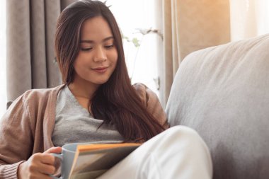 Kitap okuyan ve elinde kahve fincanı tutan genç bir kadın..