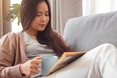 Kitap okuyan ve elinde kahve fincanı tutan genç bir kadın..