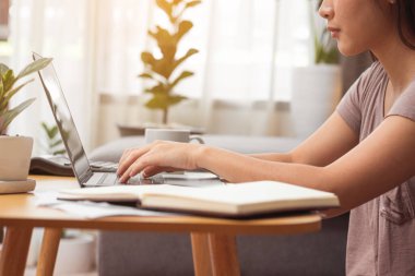 Evde çalışmak için dizüstü bilgisayar kullanan genç bir kadın.