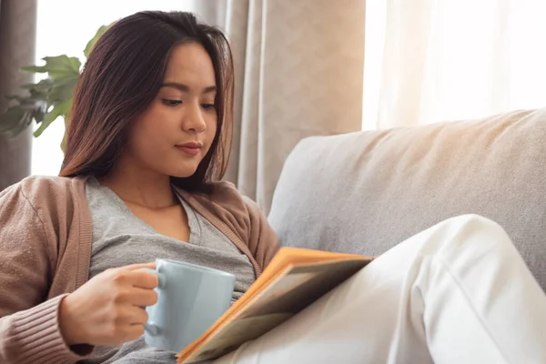 Kitap okuyan ve elinde kahve fincanı tutan genç bir kadın..