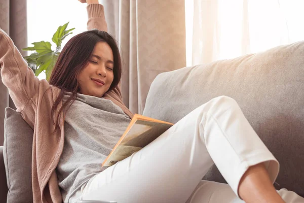 Kanepede kitap okuduktan sonra gerinen genç bir kadın.