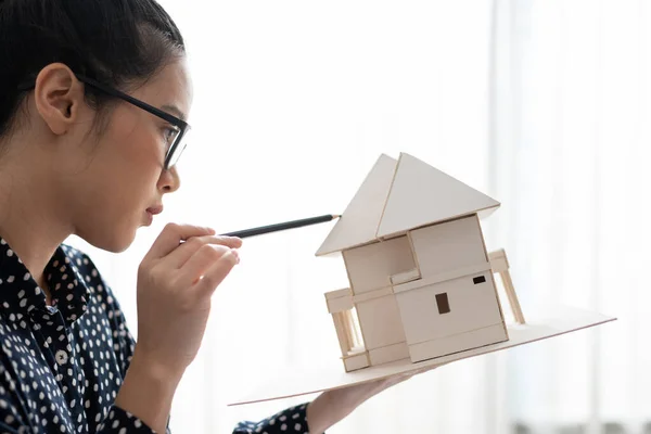 Architect woman looking at architectural model with pencil in hand.