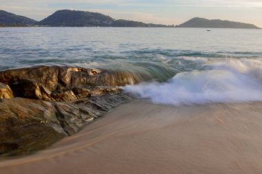 Sahilde büyük bir taşın olduğu kumlu bir sahil manzarası hangi dalgaların vurduğu, uzun pozlama.