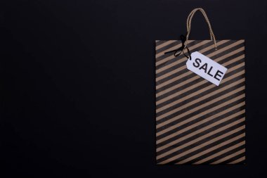 Kara Cuma konsepti. Siyah çizgili kağıt el çantası ve siyah arka planda satış etiketi. Boşluğu kopyala, üst görünüm