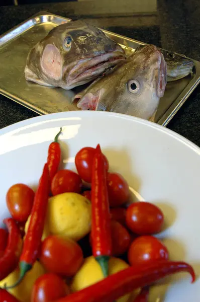 Kırmızı biber, kiraz domatesleri ve limon arka planda iki büyük morina kafası.