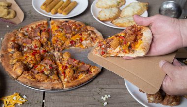 Bir dilim ızgara pizzayı karton bir kutuda teslim etmek. Pizza partisi. Ahşap arka planda İtalyan etli pizzası.