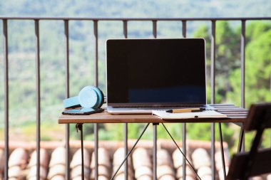Evden çalış, evin terasında portatif kulaklıklar ve not defteriyle bir masa ayarla..