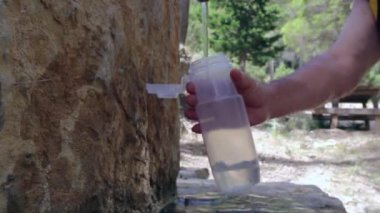 Gezgin dağ çeşmesinden şişe su döker. Turistler şişeden su içer..